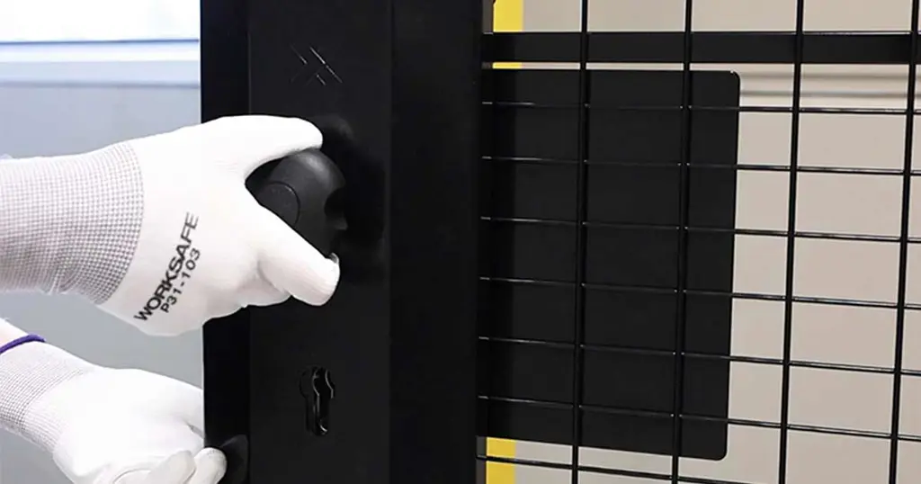 Hand holding a cylinder panic release mounted on a black mesh panel 